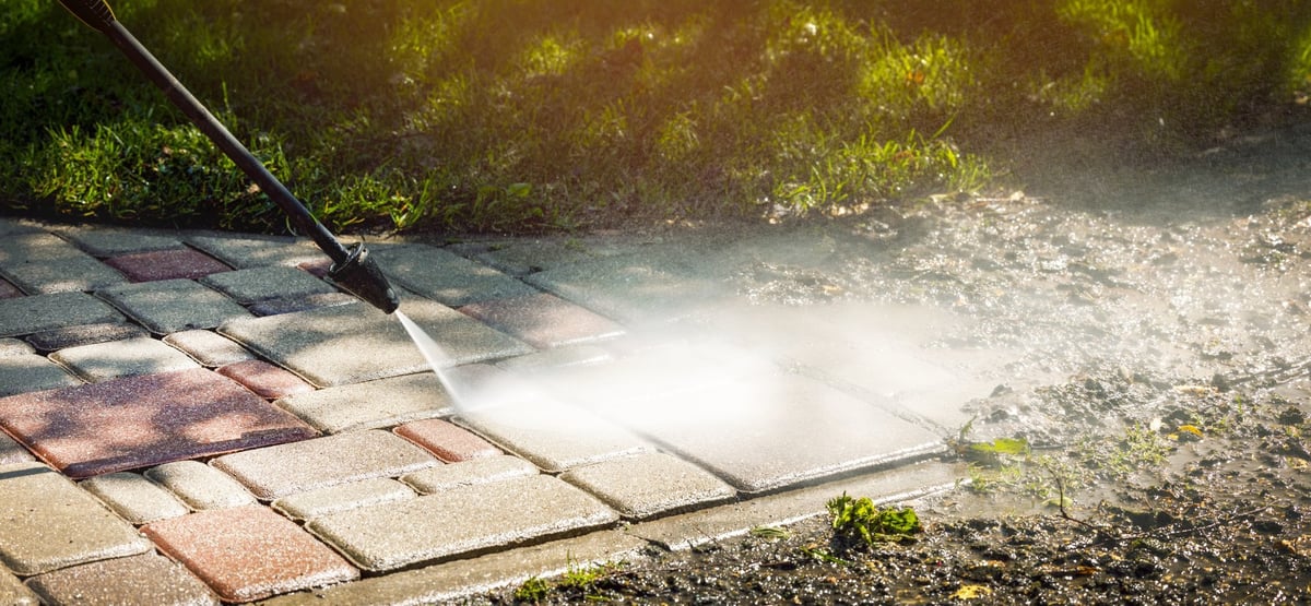 Dirty block pavement being cleaned with a high pressure washer