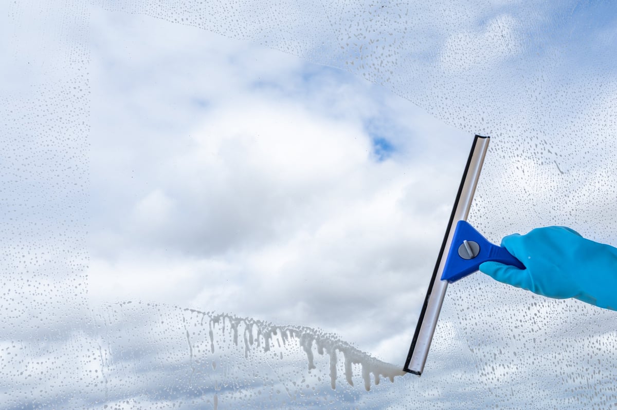 A gloved hand uses a squeegee to clean a window against a blue sky